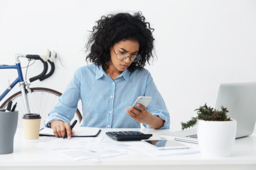 Woman looking frustrated with phone and calculator