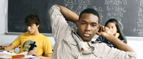 Teenage Boy Sits at a Desk in a Secondary School Classroom, Looking at the Camera With Attitude