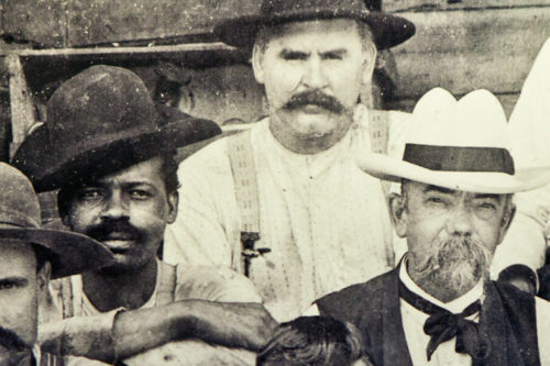 In a photo in Jack Daniel’s old office, Jack Daniel, with mustache and white hat, is shown at his distillery in Tennessee in the late 1800s. The man to his right could be Nearest Green, a slave who helped teach Jack Daniel how to make whiskey, or one of Green’s sons.