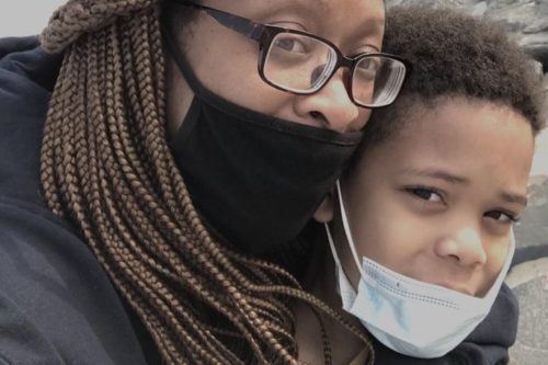 5ffca622260000da687a3dab A black woman holding her child while wearing masks.