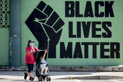 A girl in a stroller plays as a woman pushes her past a Black Lives Matter mural in the Shaw neighborhood in Washington. (AP Photo/Andrew Harnik, File)