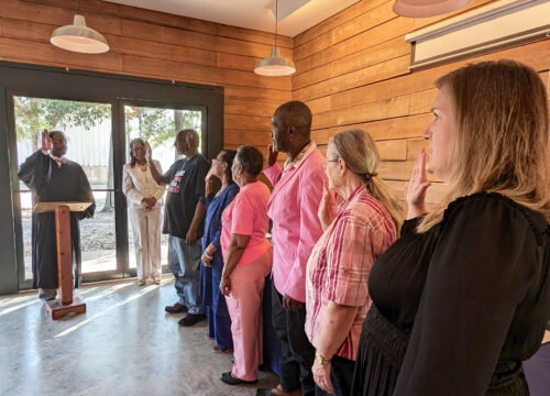 Alabama Fourth Circuit Court Judge Marvin Wiggins (at podium), along with Alabama Conference of Black Mayors Executive Director Vickie Moore, standing by the door, swears in the new council members for the town of Newbern at the Newbern town hall on Oct. 27, 2024. From left: James Robinson, Barbara Patrick, Janice Quarles, Mayor Patrick Braxton, Ann Bailey and Marla Cole. (Dwayne Fatherree)