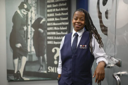 Keturah Johnson, international vice president for flight attendant union AFA-CWA, poses by a decades old, outdated poster with rules and uniforms for flight attendants, at her headquarters office, Wednesday, Sept. 18, 2024, in Washington. (AP Photo/John McDonnell)