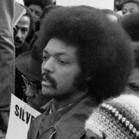 A young Jesse Jackson at a rally, sign in the background