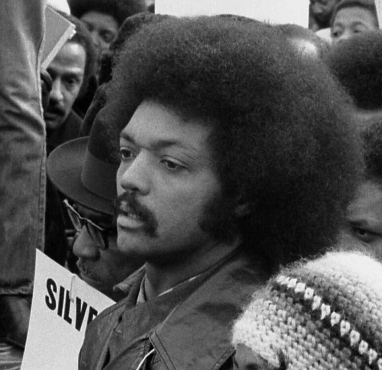 A young Jesse Jackson at a rally, sign in the background